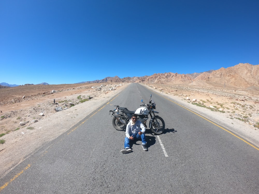 man sitting on road near motorcycle during daytime