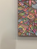 An abstract artwork featuring a multitude of geometric shapes and forms, outlined in black and filled with a spectrum of pastel colors. The textured surface adds depth and dimension, with swirling patterns and intersecting lines creating a sense of movement within the composition.