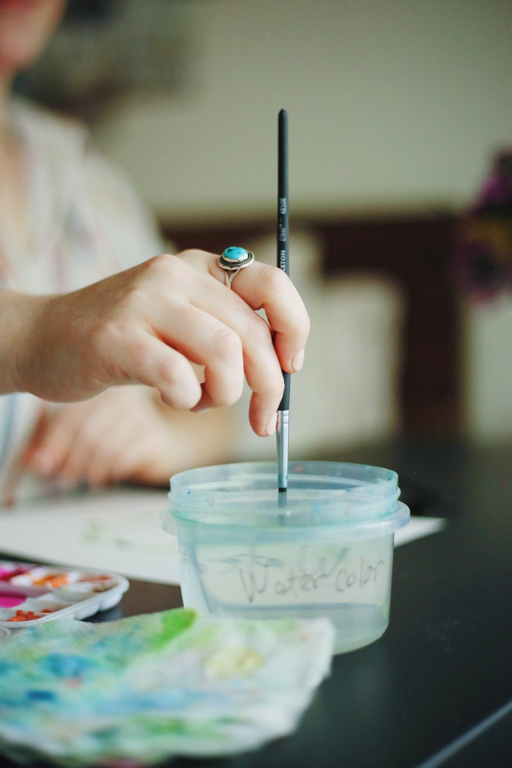 woman stirring round white plastic container with black paint brush