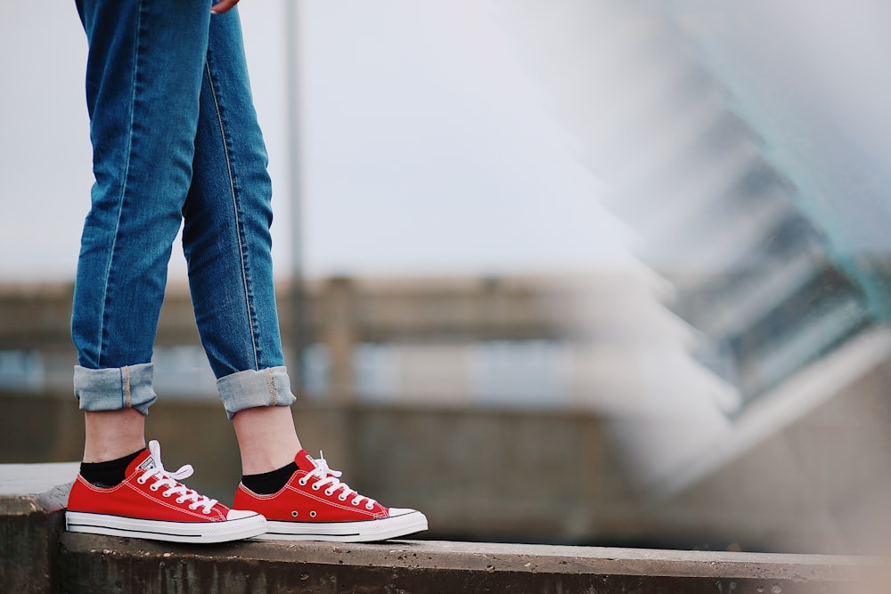 Person in roten Converse All-Star Low-Top-Sneakern steht auf dem Zaun