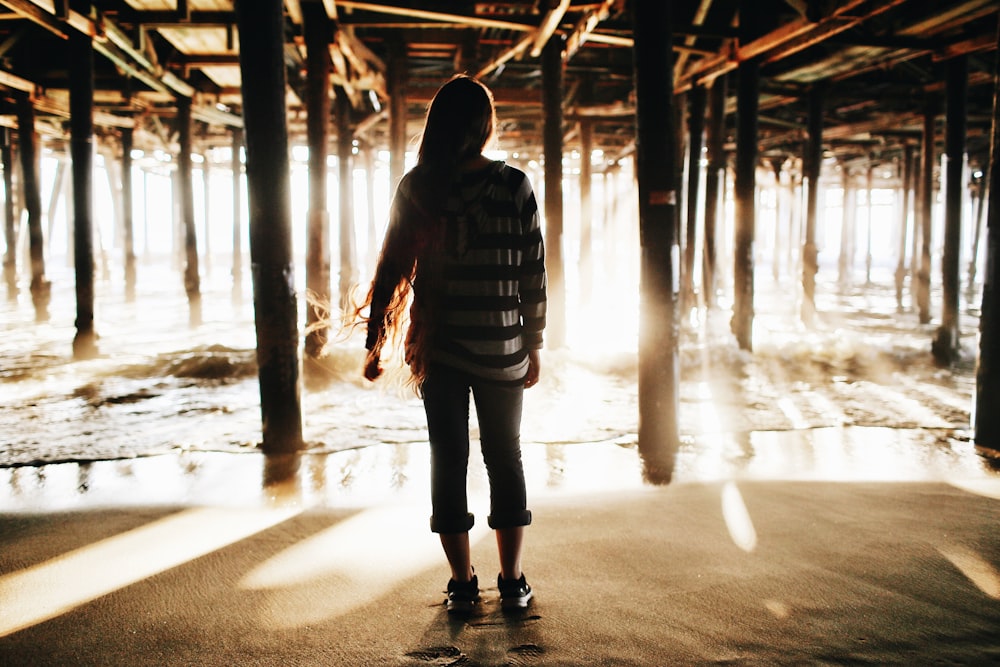 Frau steht im Sand unter Holzsteg in der Nähe des Meeres