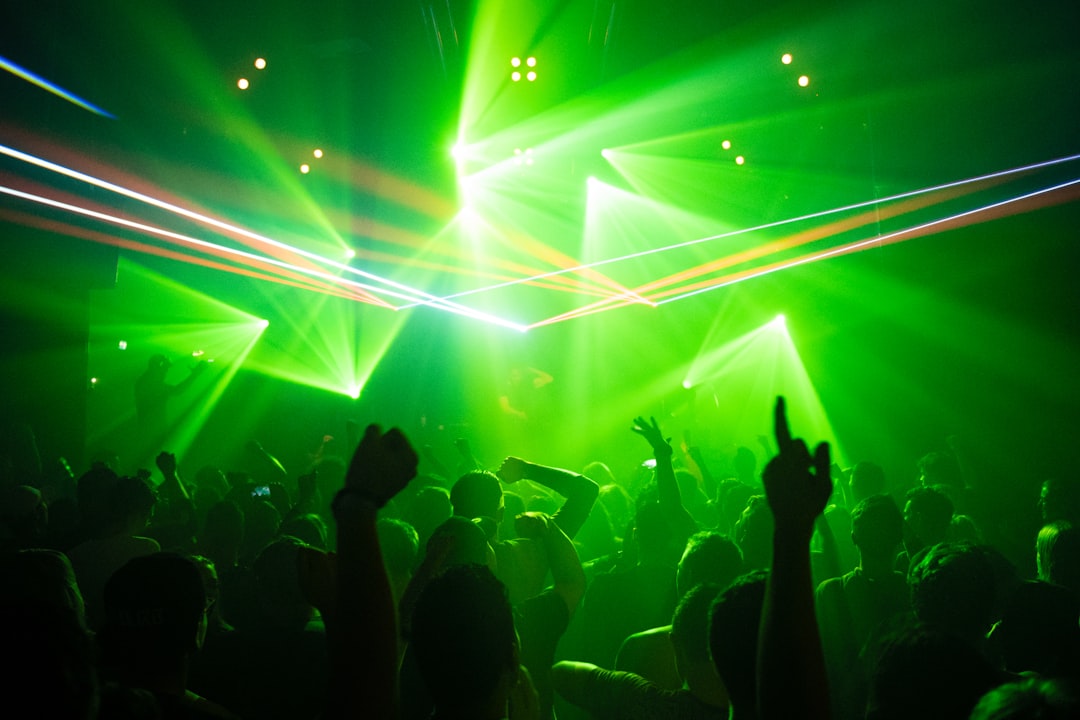 people dancing inside room with green lights, People dancing in a club while a DJ is playing electronic music with laser
