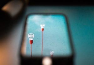 Two light bulbs with red bases are reflected on a smartphone screen. They are set against a backdrop with a turquoise hue.
