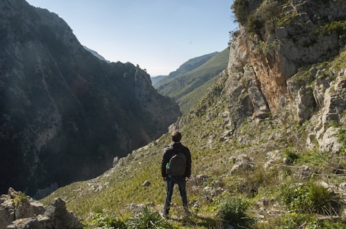 A hiker pausing on a rocky trail overlooking a sunlit valley in Israel.