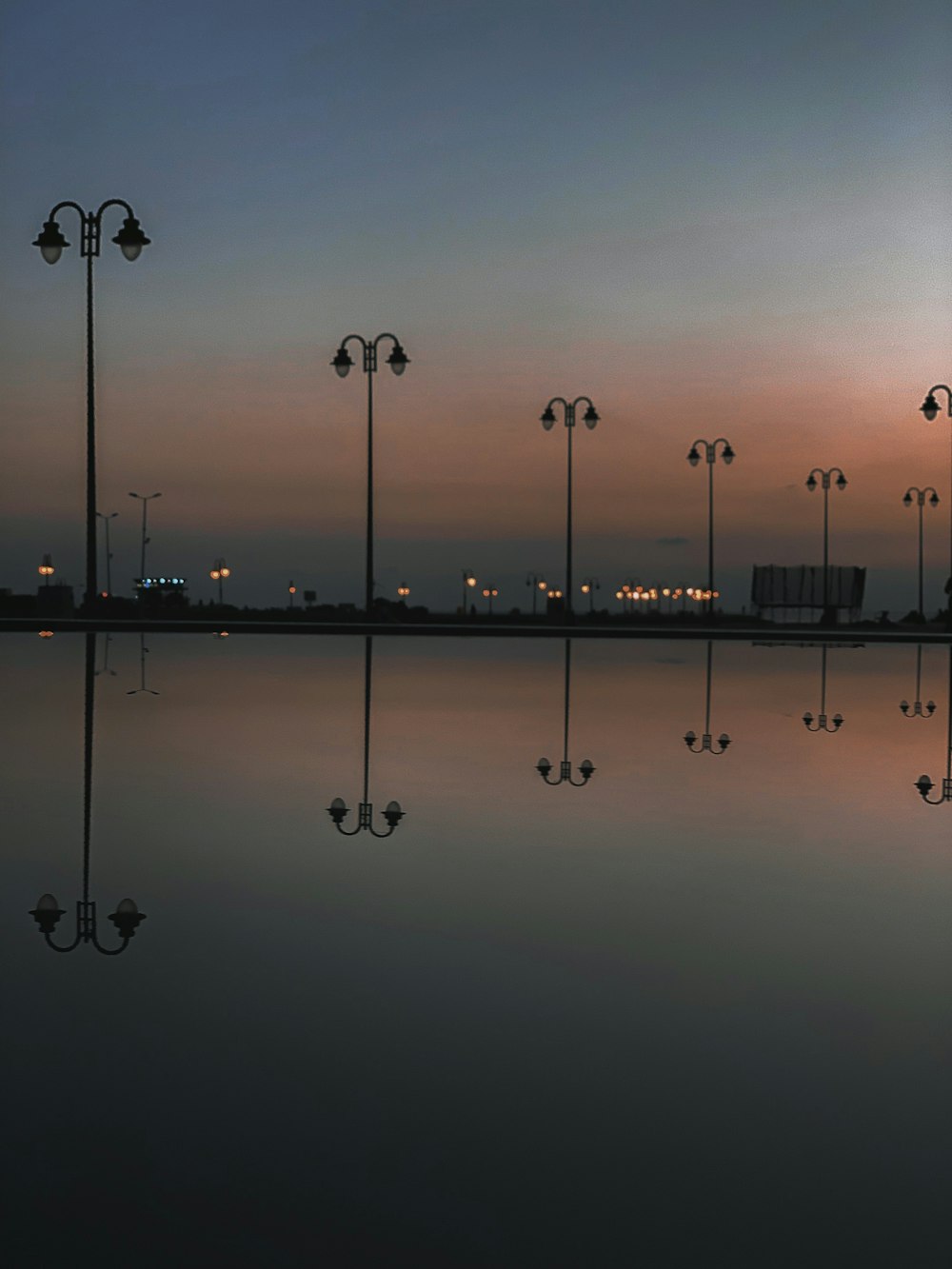 black lamp post reflection on body of water at night