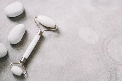 Minimalist flat lay of a jade roller and gua sha stone on a white linen cloth.