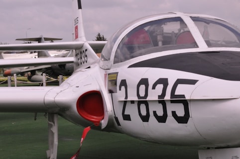 An aircraft parked on a green surface with numbers 2835 prominently displayed on its side. The cockpit is visible with a clear canopy, and part of another aircraft is seen in the background with similar livery.