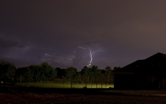 A photographer standing at a safe distance, capturing a vivid lightning strike over a dark stormy landscape.