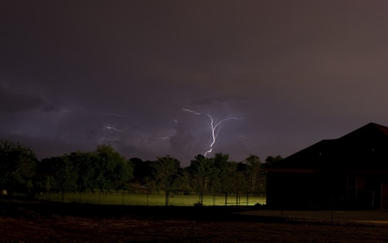 A photographer standing at a safe distance, capturing a vivid lightning strike over a dark stormy landscape.
