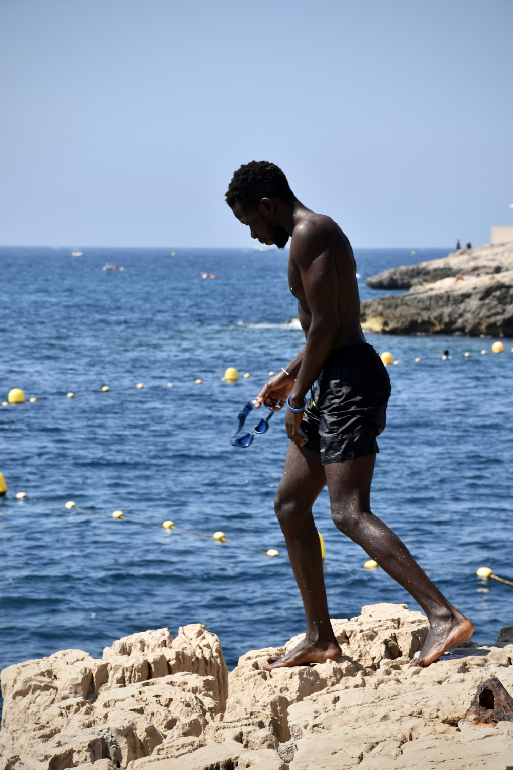 topless man standing on coastal rock during daytime