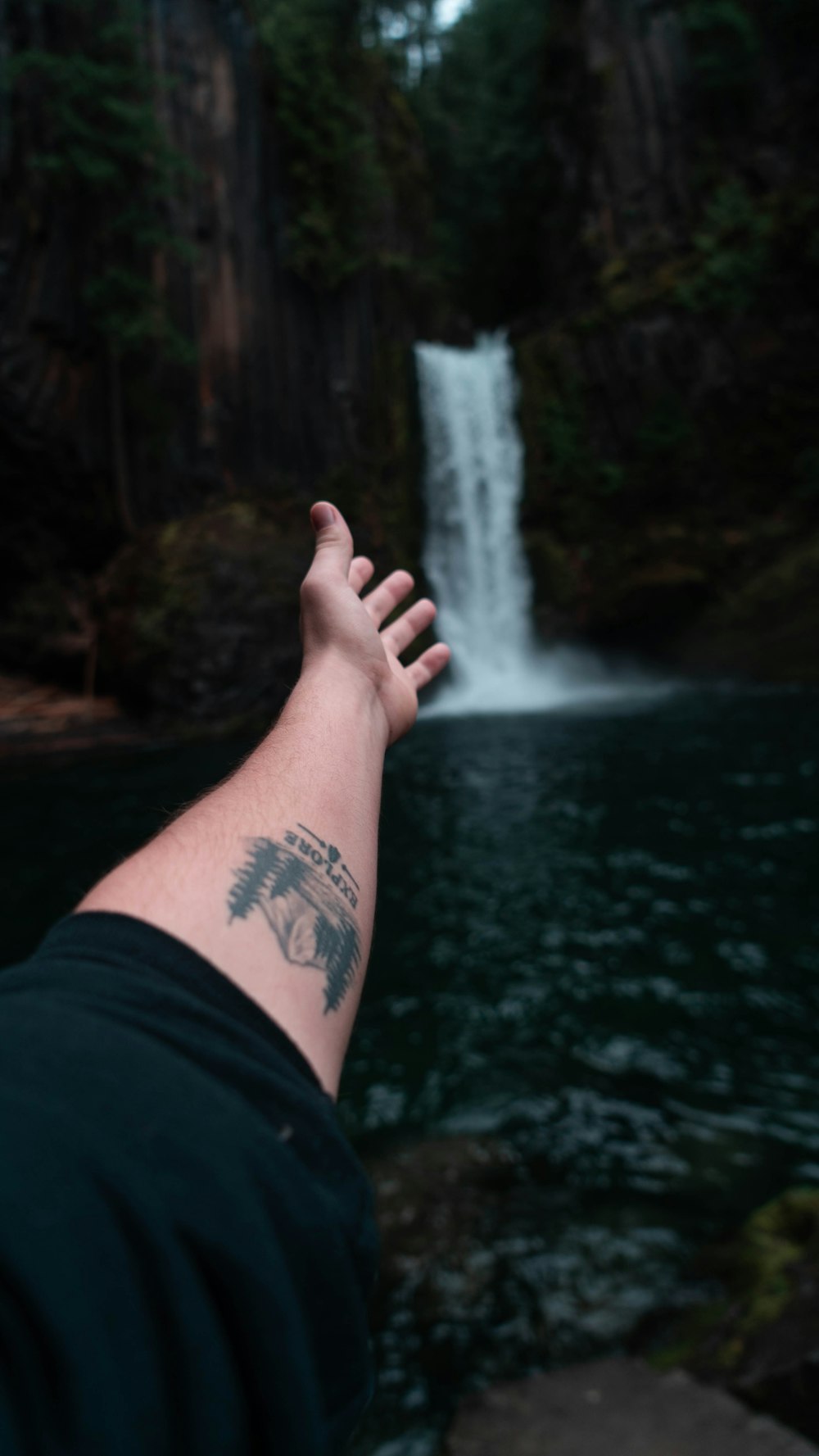 person reaching out on waterfall