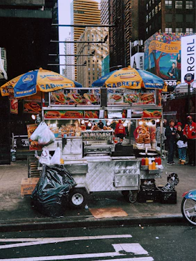 A vibrant street vendor cart with Sabrett hotdogs sizzling under a bright New York City skyline.