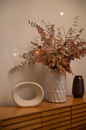 A minimalist ceramic vase holding fresh eucalyptus branches on a wooden side table.