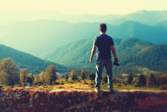 A serene mountain landscape with a lone traveler capturing the view on camera.