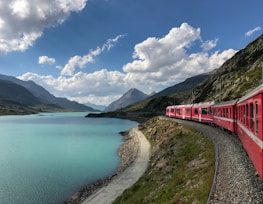 red train travelling near body of water