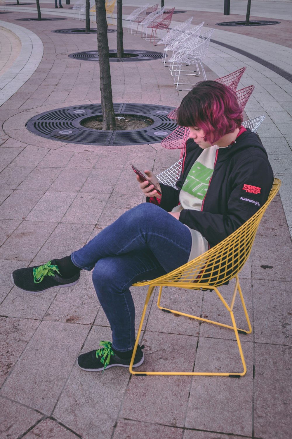woman sitting on yellow mesh-link chair holding black smartphone