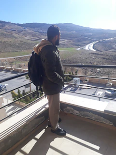 A cheerful traveler with a backpack looking at a laptop screen displaying flight deals on a sunny balcony.