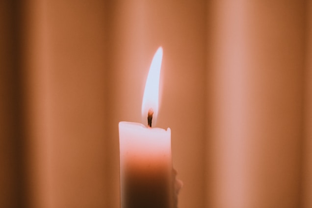 A warm, elegant candle flickering softly on a wooden table in a cozy living room.