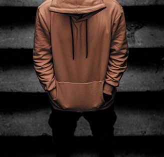 person in brown hoodie and black pants standing on staircase