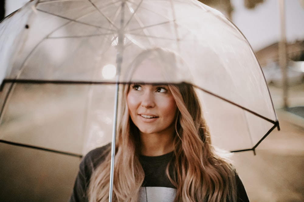Frau lächelt und benutzt tagsüber einen durchsichtigen Regenschirm
