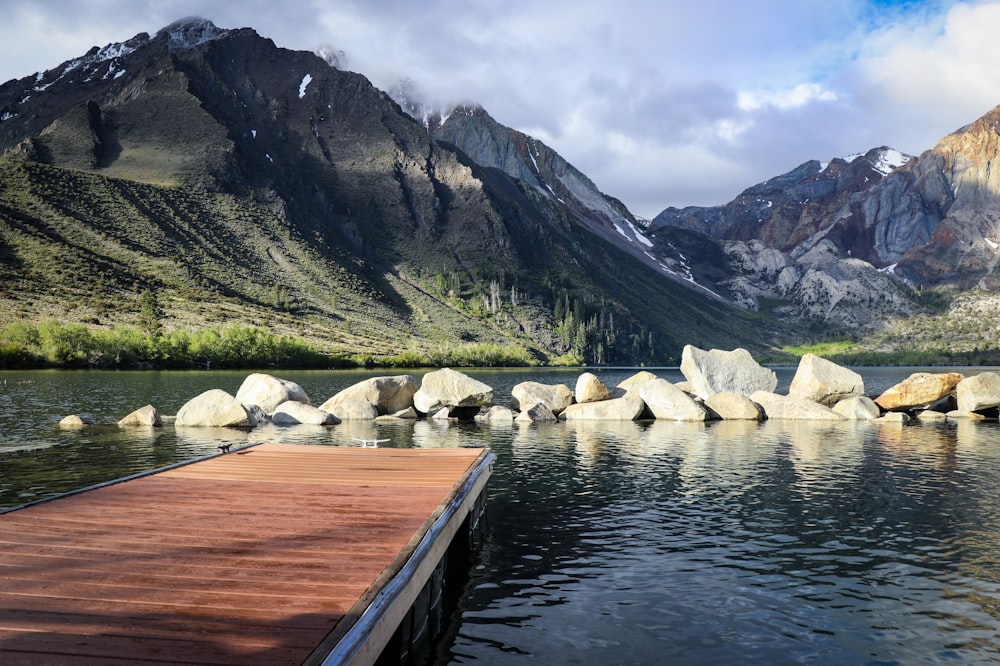 fotografia di paesaggio di rocce su specchio d'acqua e montagne verdi sotto un cielo nuvoloso