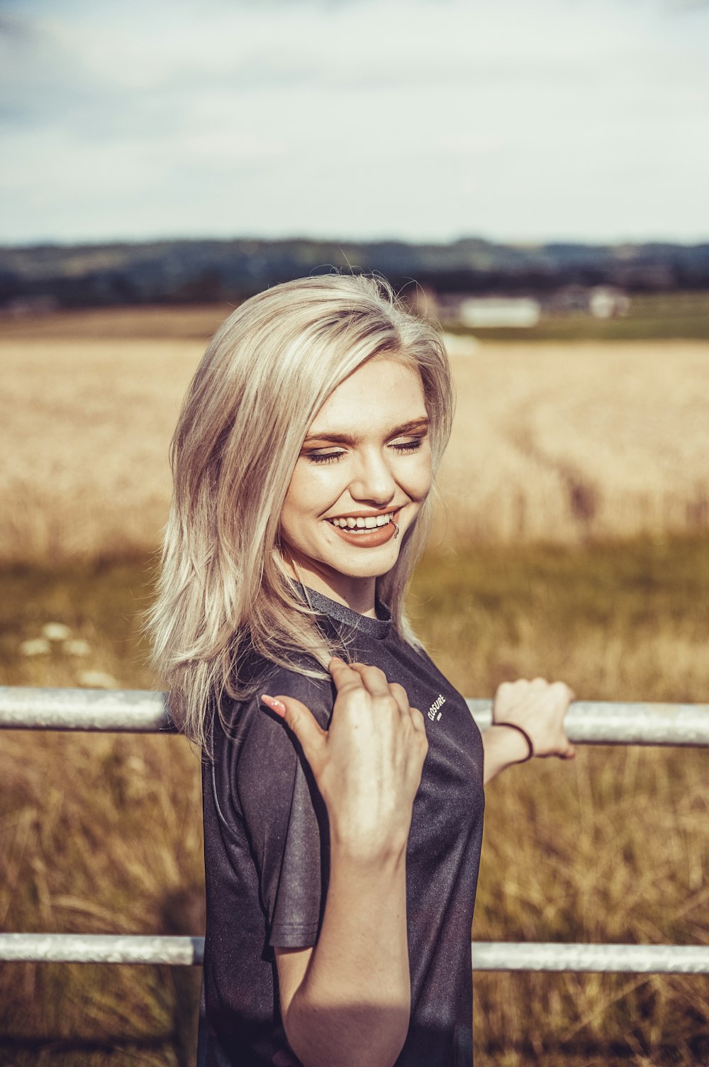 woman in black shirt leaning on gray steel fence near field