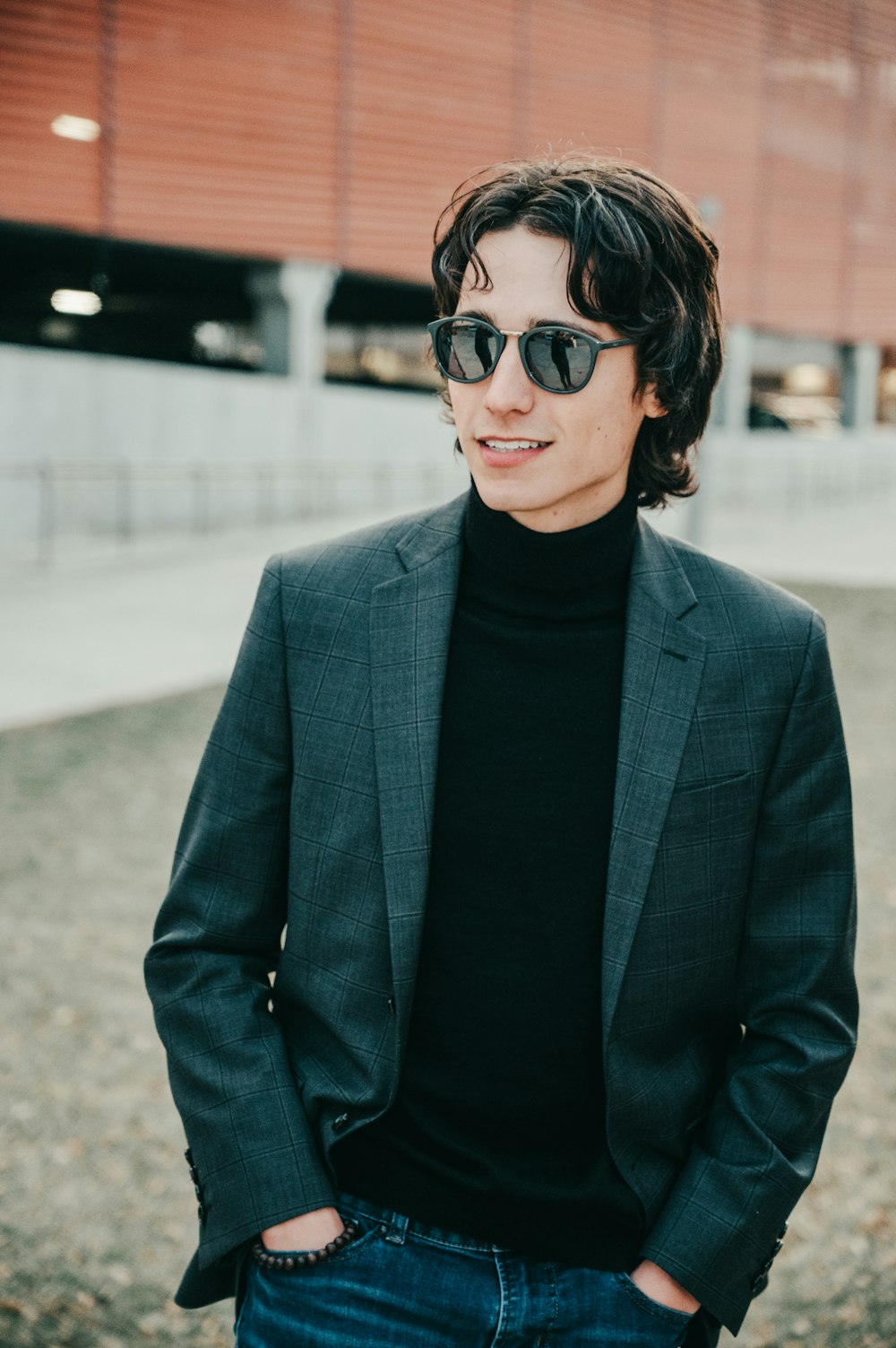 homme portant une veste de costume grise à revers cranté et des lunettes de soleil debout sur le terrain souriant