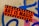 A vibrant sticker with the text 'Art is Magic' is plastered on a rough concrete wall. The sticker is orange with black stars framing bold black letters. The wall features graffiti in blue and pink spray paint, creating an urban, artistic backdrop.