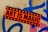 A vibrant sticker with the text 'Art is Magic' is plastered on a rough concrete wall. The sticker is orange with black stars framing bold black letters. The wall features graffiti in blue and pink spray paint, creating an urban, artistic backdrop.