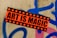 A vibrant sticker with the text 'Art is Magic' is plastered on a rough concrete wall. The sticker is orange with black stars framing bold black letters. The wall features graffiti in blue and pink spray paint, creating an urban, artistic backdrop.