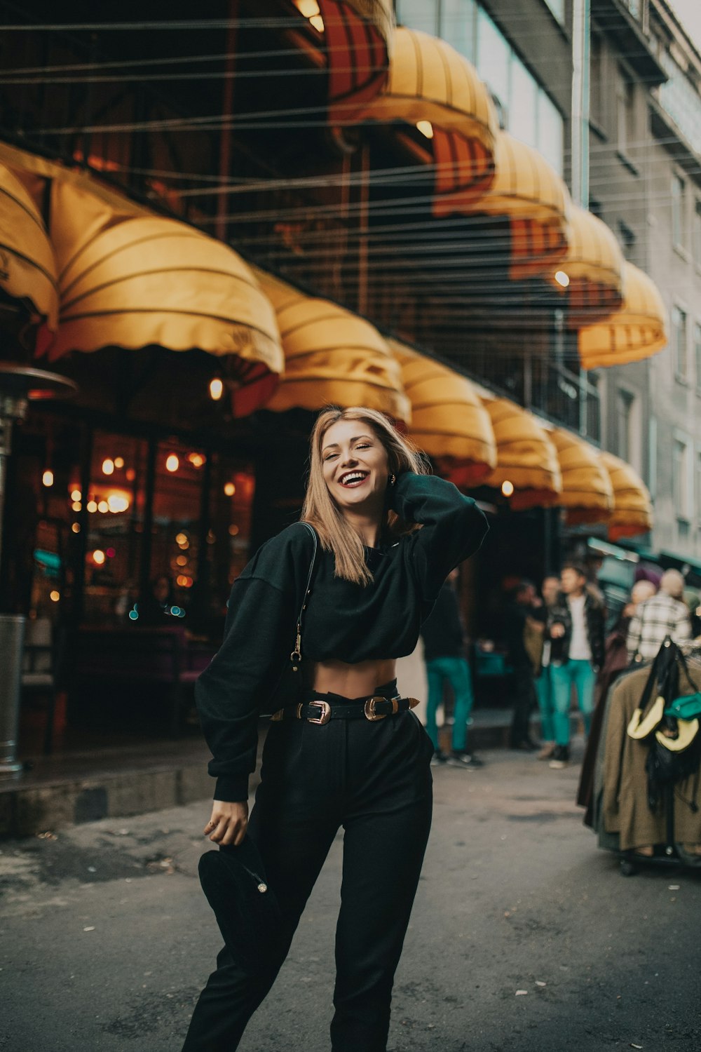 woman wearing black crew-neck sweater with shoulder bag standing on road near buildings during daytime