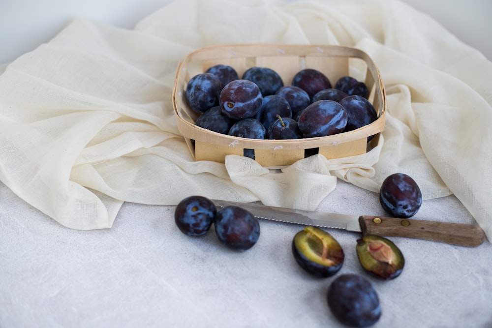 blueberry fruits in brown wicker basket near knife and white cloth
