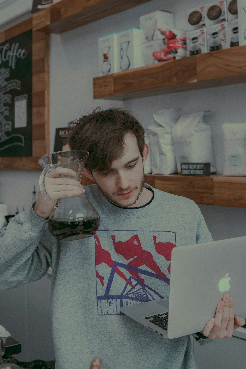 man holding clear vase on right hand and MacBook on other