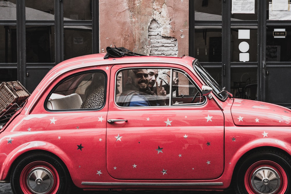 man riding on the red Volkswagen beetle