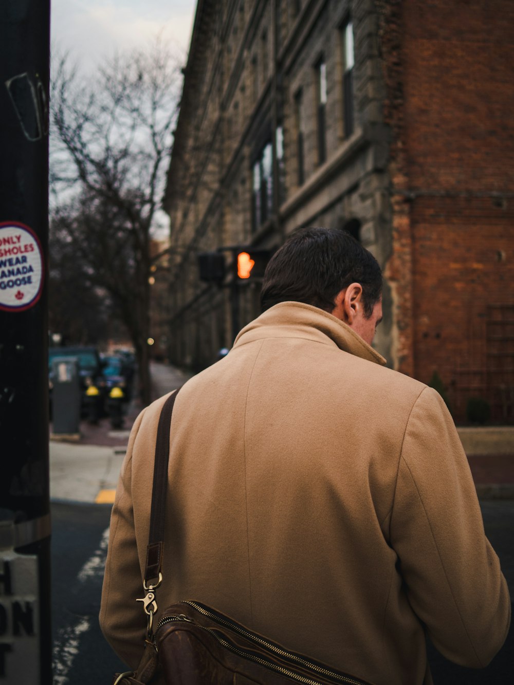 man in brown coat by bricked building at daytime