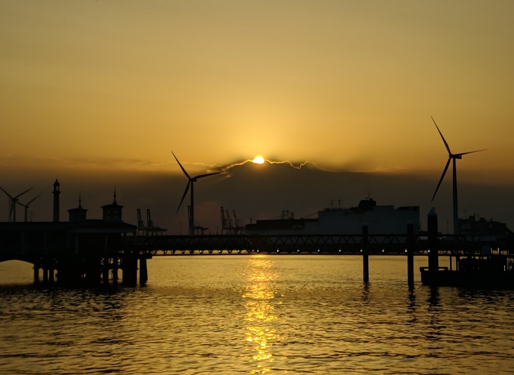 silhouette photography of windmills by the sea during golden hour