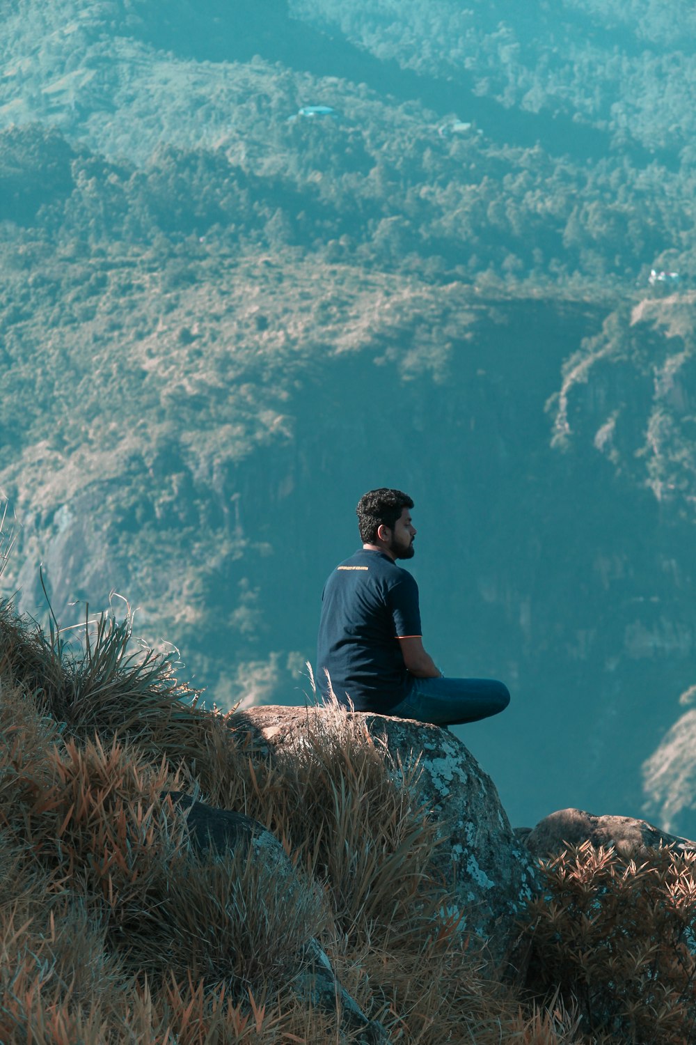man sitting atop of rock facing mountains at daytime