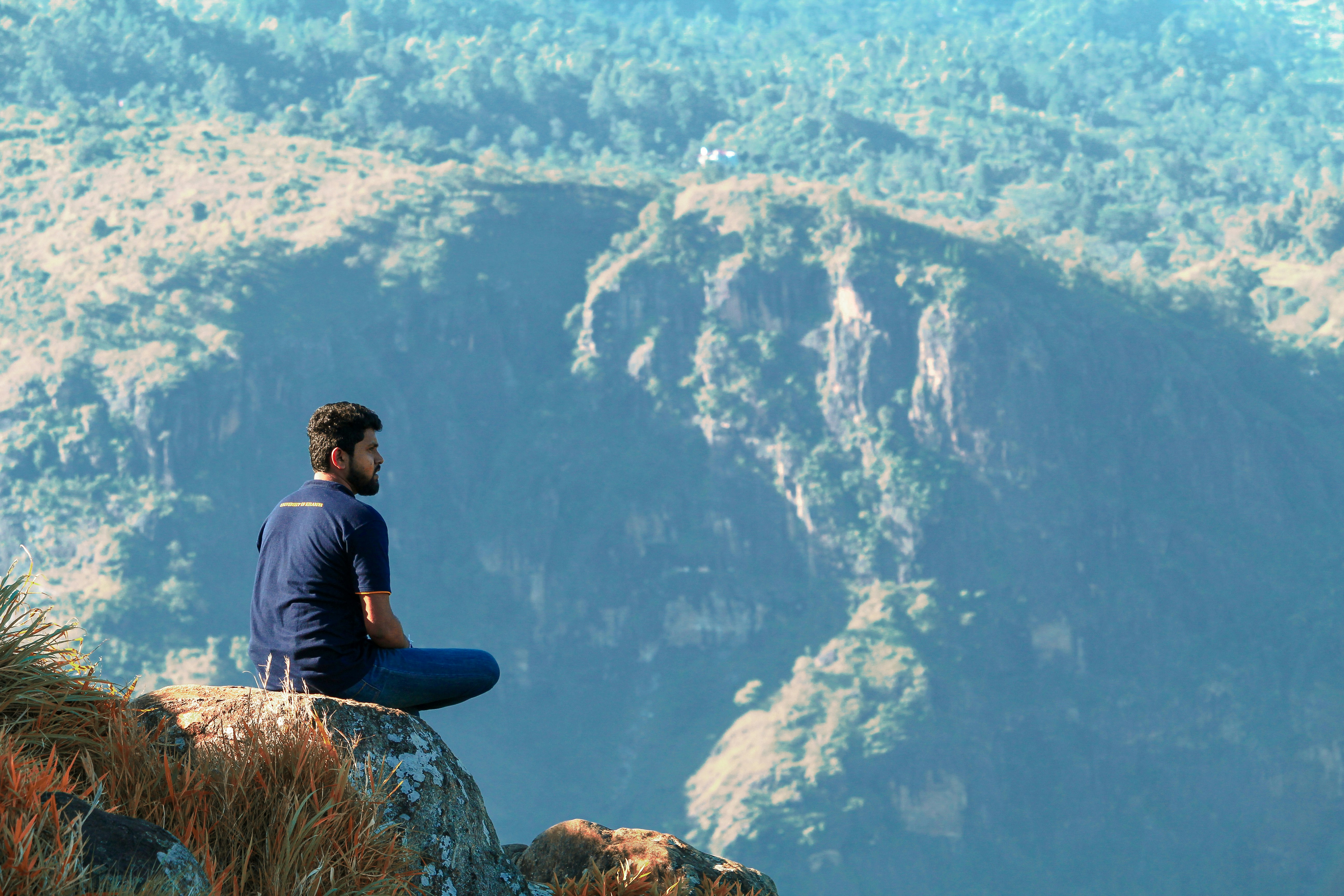 man sitting on a mountain cliff taking a photograph