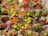 A vibrant display of colorful flowers wrapped in transparent plastic. The flowers are mainly red and yellow, surrounded by lush green leaves. The wrapping is adorned with small pink star patterns, adding a festive touch.