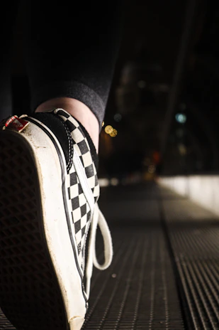 Close-up of a sleek black sneaker with white soles on a city sidewalk.