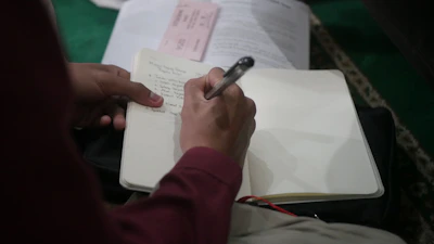 A passionate football fan sitting on a stadium bench, notebook in hand, capturing thoughts during a match.