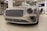 A luxury car with a sleek, metallic exterior and distinctive grille is displayed inside a modern showroom. The lighting highlights the vehicle's glossy finish and elegant design features.