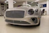 A luxury car with a sleek, metallic exterior and distinctive grille is displayed inside a modern showroom. The lighting highlights the vehicle's glossy finish and elegant design features.