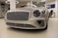 A luxury car with a sleek, metallic exterior and distinctive grille is displayed inside a modern showroom. The lighting highlights the vehicle's glossy finish and elegant design features.