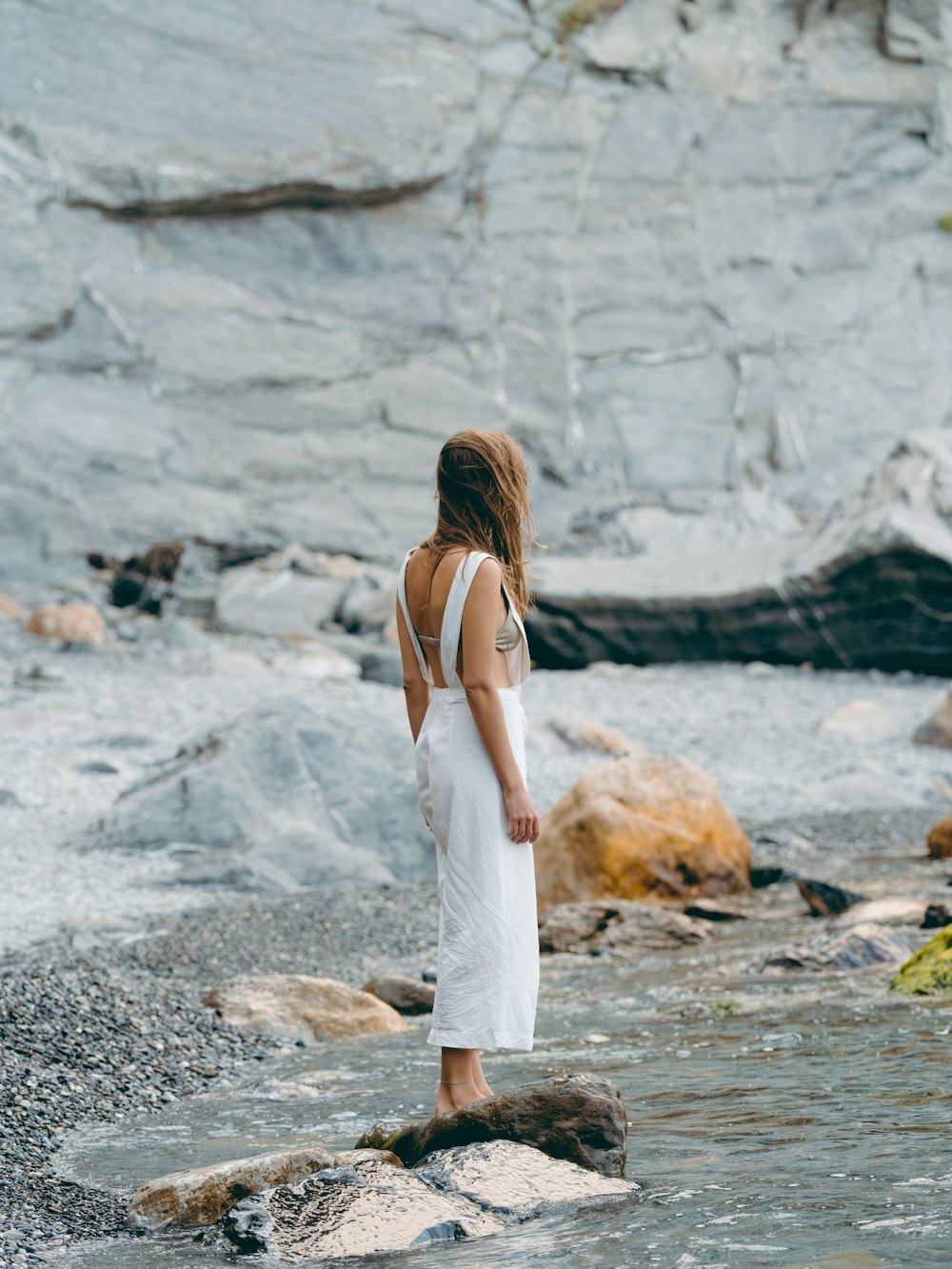 woman wearing white dress standing on the stone near the body of water