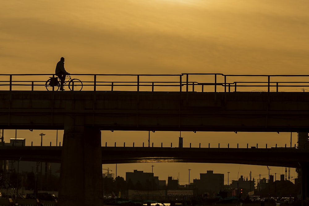 man riding bike on bridge during sunset
