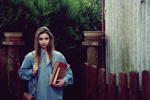 A confident young student holding books with a Canadian university campus in the background.