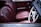 The image features a classic car interior with rich burgundy leather seats. The steering wheel is vintage in design, primarily white with metallic accents. The dashboard and door panel complement the color scheme.
