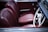 The image features a classic car interior with rich burgundy leather seats. The steering wheel is vintage in design, primarily white with metallic accents. The dashboard and door panel complement the color scheme.