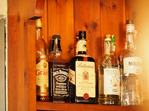 Several bottles of alcohol are lined up on a wooden shelf. Each bottle has a distinct label, indicating different types of spirits including whiskey and gin. The wood grain of the shelf adds a warm, rustic look to the image.